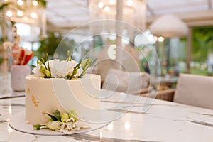 Soft focused shot of beautiful white wedding or birthday cake with roses flowers on marble table, restaurant background
