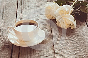 Soft full blown white roses with cup of black coffee on wooden board with copy space. Toned image. Close up.