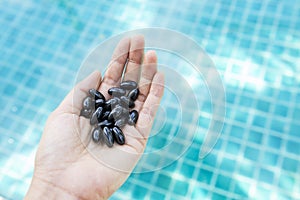 Soft gel capsule in girl hand over blurred blue swimming pool water background