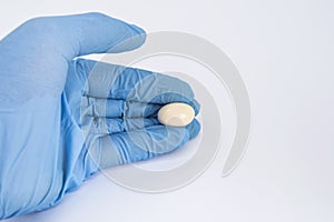 Soft gelatin vaginal tablet or suppository in the hand of the gynecologist, dressed in a blue latex glove. Treatment of diseases o