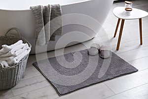 Soft grey mat with slippers on floor near tub in bathroom. Interior design