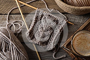 Soft grey woolen yarn, knitting, needles and glass of coffee on wooden table, flat lay