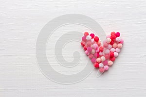 Soft heart made of fluffy pompons on white wooden background for Valentine day or Wedding