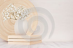 Soft home decor of beige bamboo dish and white small flowers in ceramic vase on white wood background. Interior. photo