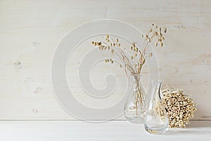 Soft home decor of glass vase with spikelets and stalks on white wood background.