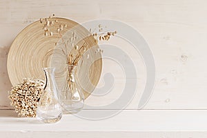 Soft home decor of glass vase with spikelets and wooden plate on white wood background.