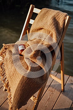 A soft knitted beige blanket lies on a wooden chair on the veranda in the country. cozy home accessories