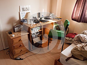 Soft light lit student bedroom desk and chair clutter messy