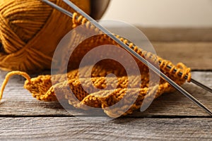 Soft orange knitting, yarn and metal needles on wooden table, closeup