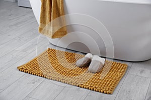 Soft orange mat and slippers on floor near tub in bathroom. Interior design