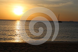 Soft panorama seascape shot of a lonely yacht silhouette in calm ocean at a beautiful yellow orange sunset on a cloudy sky with a