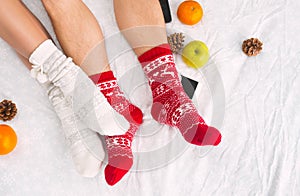 Soft photo of woman and man on the bed with phone and fruits, top view point. Female and male legs in warm woolen socks