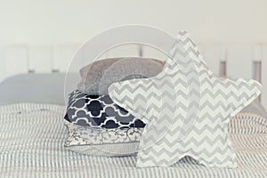 Soft pile of pillows on the edge of the bed, in gray, monochromelight background