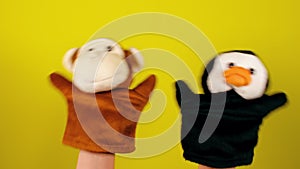 Soft puppet toys on hands on yellow background. Concept of puppet show. Close-up of hands with puppet monkey and penguin