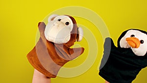 Soft puppet toys on hands on yellow background. Concept of puppet show. Close-up of hands with puppet monkey and penguin