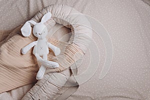 Soft rabbit toy on beige cocoon, baby nest for newborn over cribs in nursery. Childhood concept. Eco-friendly safe