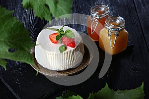 Soft ricotta cheese with strawberries, Basil leaves on a black background. Two jars of honey are next to each other on the table.