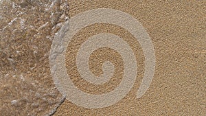 Soft sea wave covers the sand on the shore of sandy beach, top view, close up. Summer horizontal background with copyspace