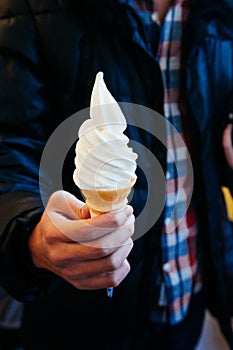 Soft serve milky vanilla ice cream cone in a man hand