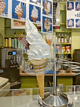 Soft serve in waffle cone place in a stainless stand in an ice cream parlor.