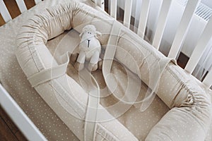 Soft sheep toy on beige cocoon, baby nest for newborn over cribs in nursery. Childhood concept. Eco-friendly safe