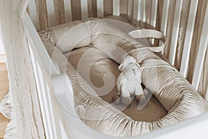 Soft sheep toy on beige cocoon, baby nest for newborn over cribs in nursery. Childhood concept. Eco-friendly safe