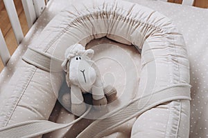 Soft sheep toy on beige cocoon, baby nest for newborn over cribs in nursery. Childhood concept. Eco-friendly safe