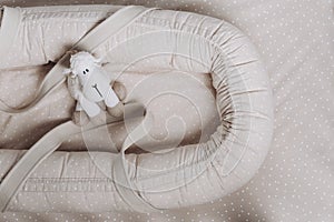 Soft sheep toy on beige cocoon, baby nest for newborn over cribs in nursery. Childhood concept. Eco-friendly safe