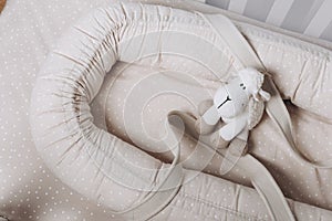 Soft sheep toy on beige cocoon, baby nest for newborn over cribs in nursery. Childhood concept. Eco-friendly safe
