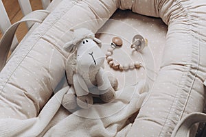 Soft sheep toy on beige cocoon, baby nest for newborn over cribs in nursery. Childhood concept. Eco-friendly safe