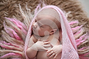 Soft sleeper newborn girl in pink on beige wool