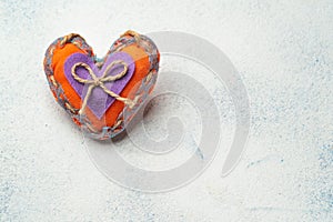 Soft stitched orange heart made of fabric with a lilac heart in the middle on a light background with an empty place for text