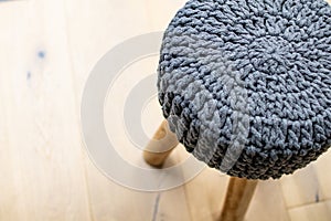 Soft stool made of wool on a light-colored wooden parquet. Stool chair with gray knitted fabric cover. Interior furnishing