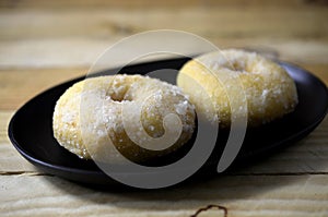 Soft sugar donut in black plate on wooden table background