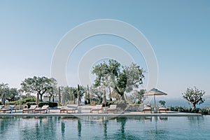 Soft sun loungers under sun umbrellas stand by the pool. Hotel Amanzoe. Peloponnese, Greece