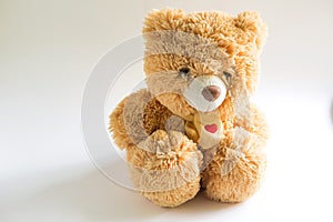 Soft Teddy bear with long light brown fur and a red heart on a scarf around his neck. Valentine`s day gift, children`s toy. White