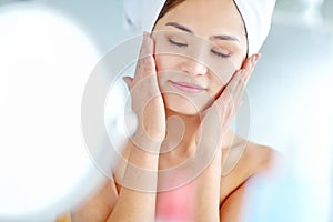 Soft to the touch. An attactive young Asian woman applying moisturizer with a towel on her head.