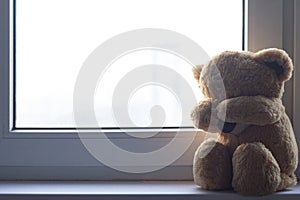 A soft toy bear cries sitting on a windowsill. There are noises in the photo, because the photo photo