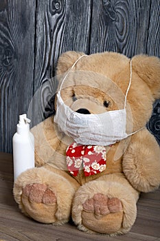 Soft toy, bear, in a protective gauze mask. In hand a spray bottle with a disinfectant. Against the background of brushed boards.