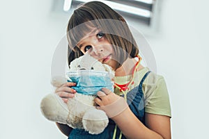Soft toy bear with protective medical mask in child hands.