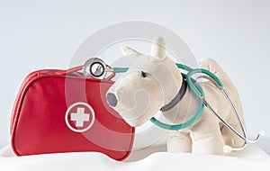 Soft toy doggy on a white background with first aid kit and stethoscope