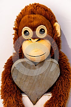 A soft toy monkey hangs on a wooden heart close up