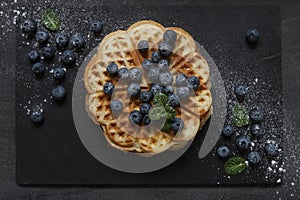 Soft Viennese waffles with blueberries sprinkled with icing sugar Top view, close-up on a dark concrete background