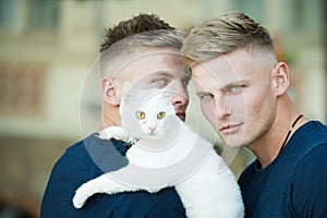 Soft and warm embrace. Muscular men with cute cat. Happy cat owners on walk with pet. Twins men hold pedigree cat. Happy