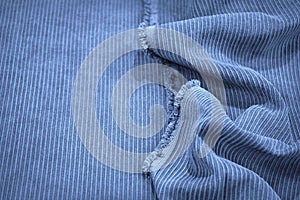 Soft wavy folds on the corduroy. Durable ribbed fabric. Close-up. Detail. Blue fabric backdrop with copy space