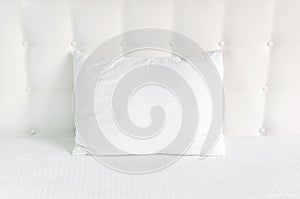 Soft white quilted pillow in bed on the background of white leather quilted headboard. Clean pillow, part of bed close-up, comfort