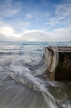 Soft white wave hitting concrete structure on the beach.