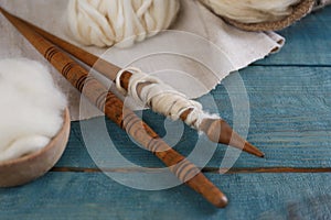 Soft white wool and spindles on blue wooden table, closeup