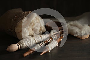 Soft white wool and spindles on wooden table, closeup