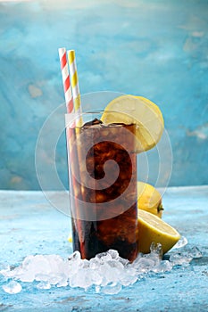 Softdrink with ice cubes, lemon and straw in glass.